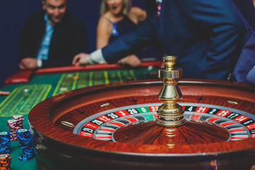 A close-up vibrant image of multicolored casino table with roulette in motion, with casino chips. the hand of croupier, mone and a group of gambling rich wealthy people in the background