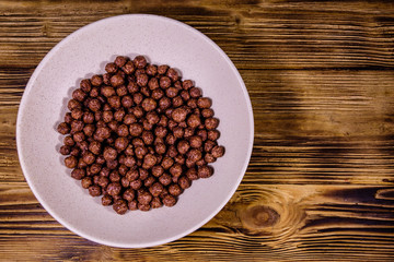 Ceramic plate with chocolate cereal balls on wooden table. Top view