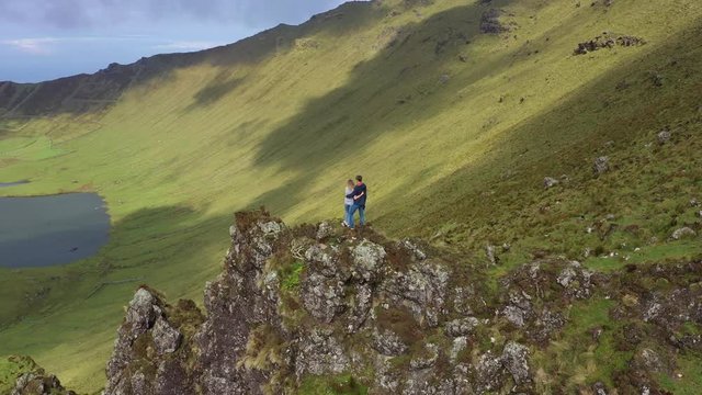 Young couple on the top of rock on the edge of caldera. Caldeirao volcano, Corvo, Azores