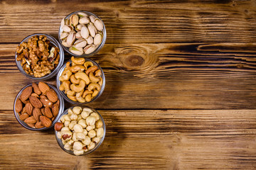 Fototapeta na wymiar Various nuts (almond, cashew, hazelnut, pistachio, walnut) in glass bowls on a wooden table. Vegetarian meal. Healthy eating concept. Top view