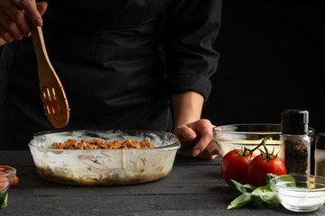Cooking an Italian dish by a chef on a background of ingredients. Freezing in motion. Sprinkles with lasagna meat.