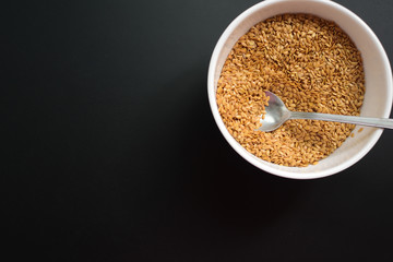 Bowl of flaxseeds with spoon over black background from above