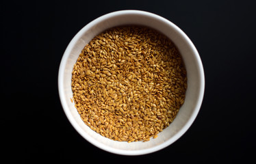 Bowl of flaxseeds with spoon over black background from above