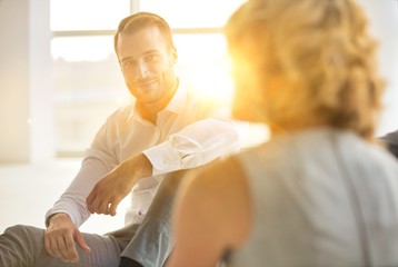 Obraz premium Handsome young businessman smiling while sitting on the floor with collegues in new office