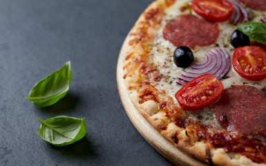 Pizza with salami, mozzarella cheese, cherry tomatoes, black olives, red onion and oregano. Home made food. Concept for a tasty and hearty meal. Black stone background. Close up. 