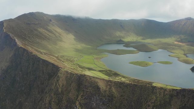 Lake in green lined caldera of huge volcano. Caldeirao top in clouds. Aerial of Corvo, Azores