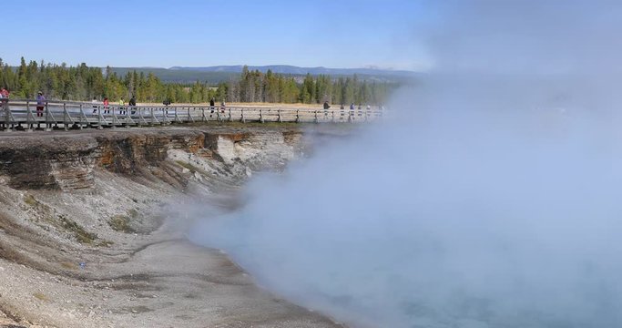 Yellowstone National Park tourist on boardwalk over geyser steam. Geyser Yellowstone National Park in Wyoming, United States. Highly predictable geothermal ecosystem feature.