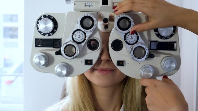 Oculist is regulating phoropter to check sight of happy smiling woman.
