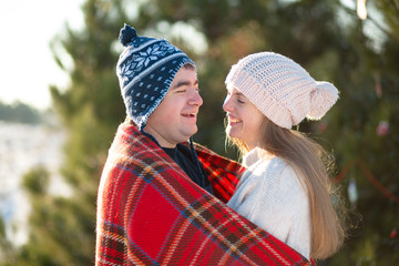 Fototapeta premium Winter walk through the woods. The guy in the red plaid blanket wraps the girl up so she gets warm