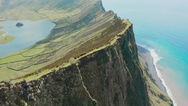 Woman walks along the edge of steep cliff of huge inactive volcano. Aerila of Caldeirao, Corvo, Azores