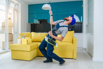 Funny male cleaning worker in special blue clothes playing with a mop as a guitar like a rockstar in the stylish cuisine. Having fun at workplace.