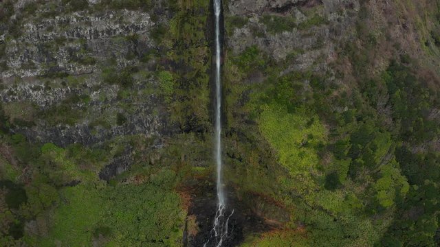Stream of Bacalhau waterfall falls from a gorge on a top of rocky mountain. Aerial of Flores, Azores