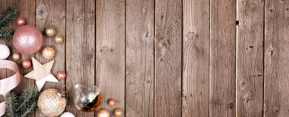 Obraz na płótnie Canvas Christmas corner border banner of dusty rose, gold and white ornaments with branches. Top view on a rustic wood background with copy space.