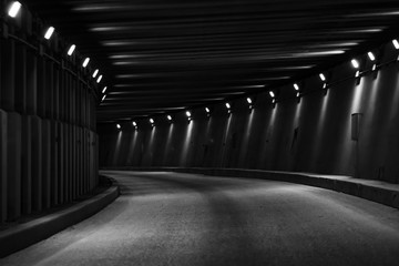 Black and white photo of a Curve tunnel for automobiles. Empty engineering construction with rhythm of lights and structure. Highway infrastructure. 