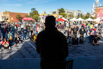 Silhouette of man talking to crowd at open public space. People standing and sitting listening to...