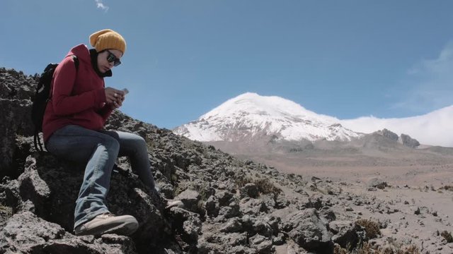 Female hiker looking at her smartphone with the Andean mountain range background, Chimborazo, Ecuador. 4k