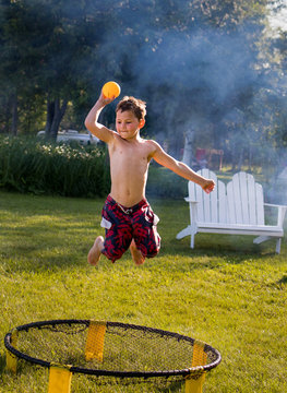 Young boy jumping and playing spike ball with smoke from bonfires in the background
