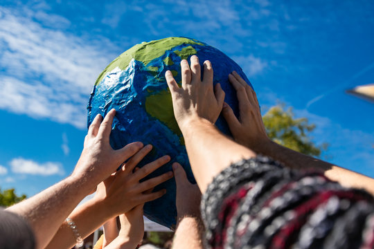 group of hands holding and protecting terrestrial globe as a symbol of environmentalism. Activist expresion of protest with cloudy blue sky