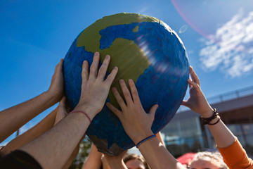 Close up of group of hands holding and protecting terra globe with lens flares. Activist expresion...