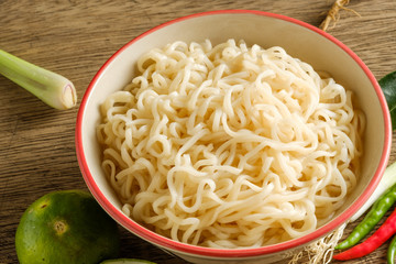 A cup of instant noodles placed on a wooden table With lime,chilli, and garlic as ingredients