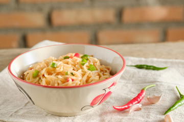 A cup of instant noodles placed on a wooden table With chilli as ingredients