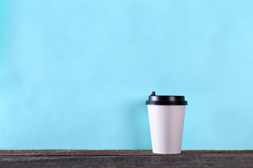 Coffee cup for take out on wooden table over blue background