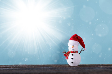 Snowman toy in Santa Claus hat on wooden table over blue background