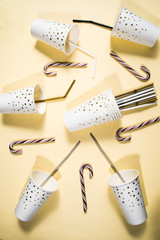 New year party theme conceptual image, top view of flat layout composition of paper glass with golden decoration, candy canes, and golden bottles of champagne and  straws empty, on a yellow background