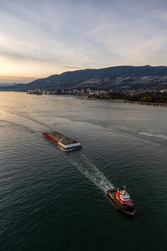 West Vancouver, British Columbia, Canada. Aerial View of a Tugboat in a modern cityscape on the Pacific Ocean Coast during an Autumn sunny and cloudy sunset.