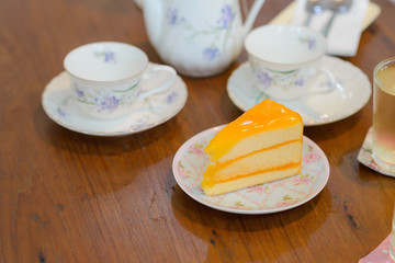 piece of delicious orange cake with teapot and cup of tea on wooden table