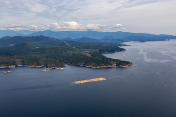 Obraz premium Aerial View of Tugboat towing Lumber in the ocean with mountain landscape in the background during a hazy summer day. Taken in Sunshine Coast, BC, Canada.