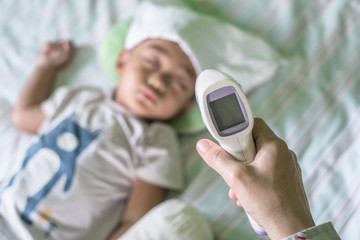Mother hand holding digital infrared thermometer to measure for her son illness and flu fever while...