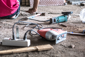 Selective focus of angular grinder and blurred jigsaw with electric wire plugged in socket and worker at construction site