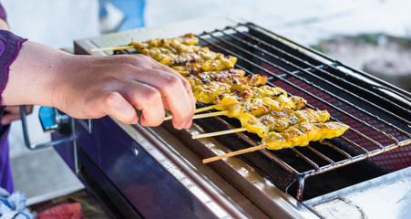 Close up of seller's hand grilling chicken in bamboo stick on electric stove. Thailand street and local food