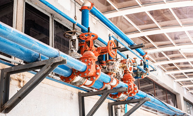 Pipe system with blue pipes and red valves on building ceiling. Water drainage pipes concept.