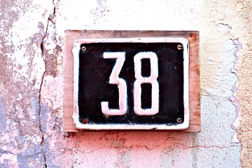Number 38, thirty-eight, metal plate with digits on a grungy old wall.