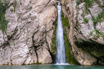 A high waterfall falls from a cliff into a clear lake