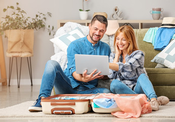 Couple with laptop and luggage planning their vacation at home