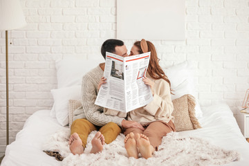 Beautiful young couple reading newspaper on bed at home