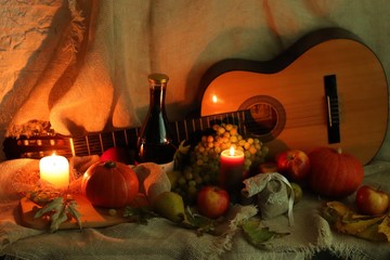 Wine and guitar. Apples, grapes and pears with pumpkins and leaves with candles flame standing on table with sackcloth