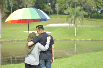 Romantic muslim couple dating expect rainy weather hold colorful umbrella on outdoor summer park.