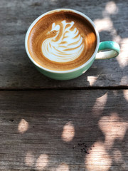 Swan shape latte art coffee in white and green cup on wooden table with natural light ; love coffee, Top view and copy space.