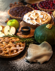 A cherry, apple, creme and nut pies on a dark wooden table with season decoration