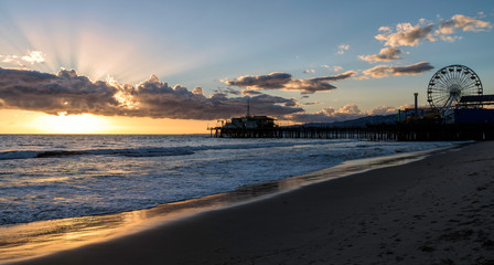 Silhouette of the Santa Monica Pier in California as the sun sets turning the ocean gold.