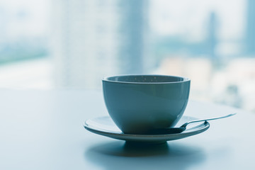 Coffee​ or tea​ cup​ blue color​ on the white​ table through the glass window of a tall building​ background, Business person's break time, Perspective of office lifestyle in big city.