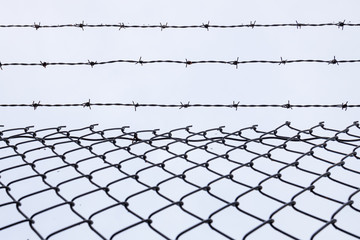 Chainlink fence with three strands of barbed wire on top. Close up and isolated against the sky