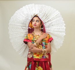 Mexican girl with a floral dress from Oaxaca Mexico, hidden in a red background with braided flowers and gold necklaces, for Mexican culture dance