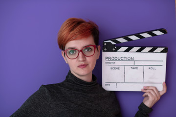 redhead woman holding movie  clapper on purple background