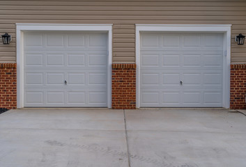 White electronic garage doors on a double garage driveway with beige horizontal lap vinyl siding and red brick accent on a new construction luxury American single family home in the East Coast USA © tamas