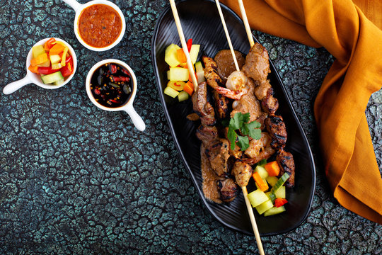 Asian meat and chicken skewers with dipping sauces and vegetables, satai or satay